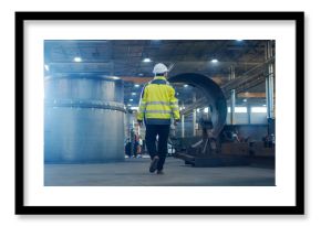Industrial Engineer in Hard Hat Wearing Safety Jacket Walks Through Heavy Industry Manufacturing Factory with Various Metalworking Processes.