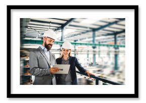 A portrait of an industrial man and woman engineer with tablet in a factory, working.