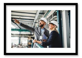 A portrait of an industrial man and woman engineer with tablet in a factory, working.