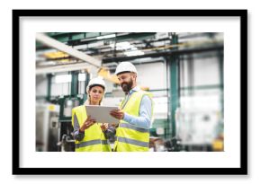 A portrait of an industrial man and woman engineer with tablet in a factory, talking.