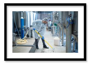 Professional industrial cleaner in protective uniform cleaning floor of food processing plant. Cleaning services.