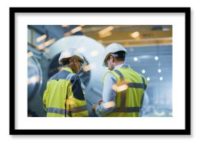 Two Heavy Industry Engineers Stand in Pipe Manufacturing Factory, Use Digital Tablet Computer, Have Discussion. Construction of Oil, Gas and Fuels Transport Pipeline. Back View Sparks Flying