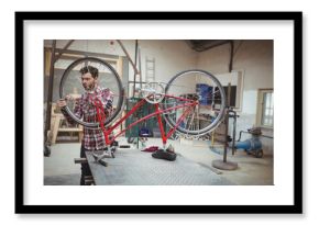 Bike mechanic tightening bolts on upside-down red bicycle at metal workbench in industrial workshop