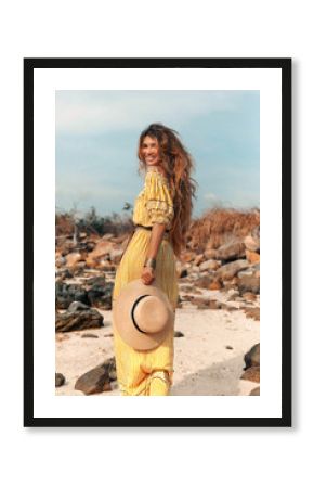cheerful young stylish woman in elegant dress outdoors wearing hat havinf fun at sunset