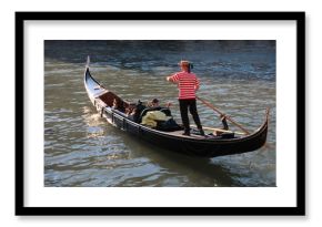 Gondola and gondolier in Venice / A typical and iconic image of Venice, Italy, a Gondolier leads his gondola with two tourists on a beautiful sunny day