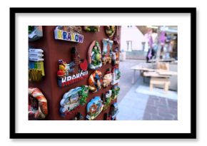 Tourist in christmas market checking a display of colorful ceramic fridge magnets featuring hand-painted depictions of Kraków, Poland, arranged on a metallic surface 