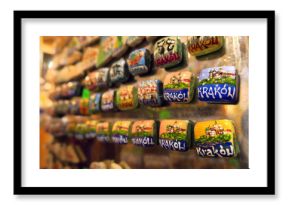 Tourist in christmas market checking a display of colorful ceramic fridge magnets featuring hand-painted depictions of Kraków, Poland, arranged on a metallic surface 