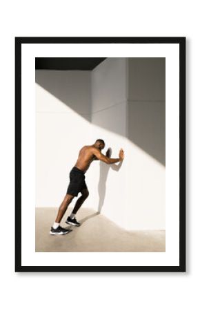 A young athlete with a naked torso performs push-ups from the wall