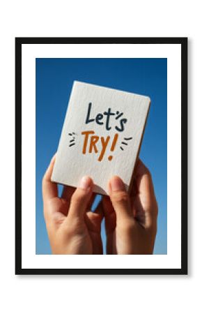 Hands hold small card against sunny blue sky, text reads "Let's Try!", conveying encouragement and motivation