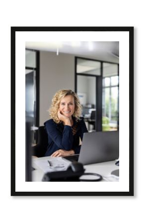 Smiling businesswoman with head in hand sitting at desk in office