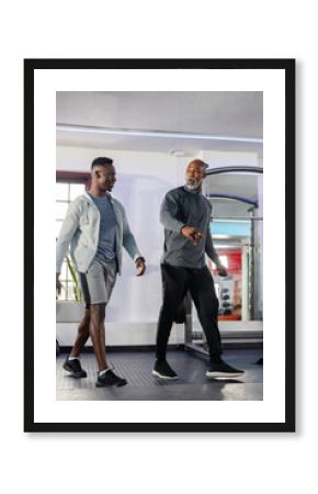 African American men walking in gym by squat rack with weight plates while coach gesturing