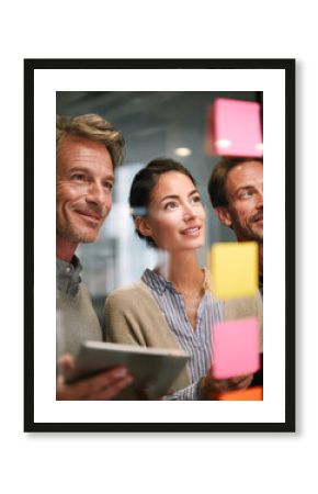 Three professionals collaborate enthusiastically in front of a glass wall with colorful sticky notes, brainstorming ideas in a modern office setting.