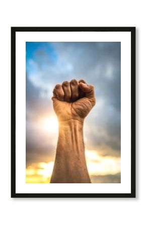 Raised fist in protest against a dramatic sunset sky symbolizes strength and determination