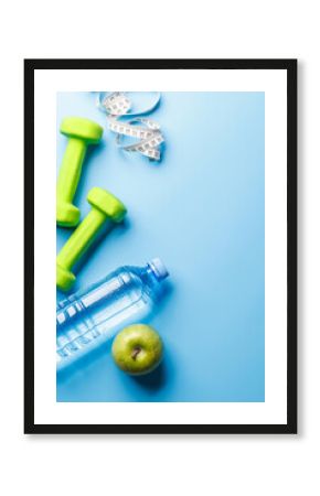 Flat lay of dumbbells, water bottle, and green apple over a bright blue