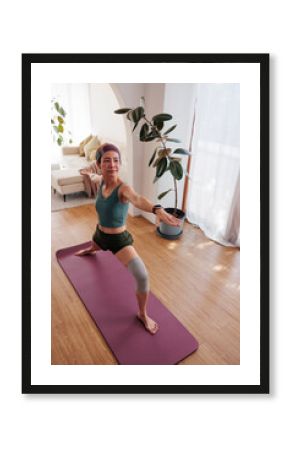 Woman in warrior pose on yoga mat at home.
