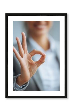 A cheerful woman makes an OK sign with her fingers, expressing approval and satisfaction in a business context.