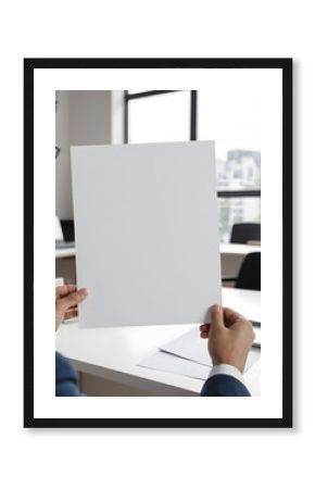 Person holding blank paper in bright modern workspace.