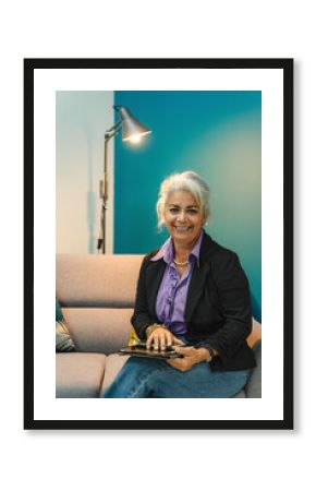 Portrait of a smiling, mature professional woman seated on a modern sofa, holding a tablet.