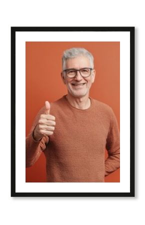 Smiling mature man in sweater giving thumbs up against orange, symbolizing success and approval. Ideal for health, finance, and positive lifestyle content.