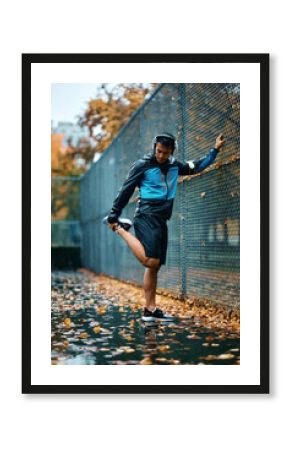 Young  sportsman stretching his leg after running in park during rainy day.