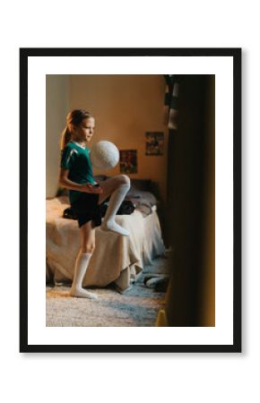 Female athlete playing with soccer ball standing in bedroom at home