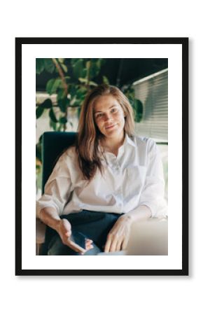 Testimonial portrait of a business woman sitting in a chair in the office with a mobile phone.