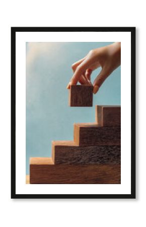 Hand placing wooden cube atop staircase against sky backdrop, symbolizing growth, progress, or achievement