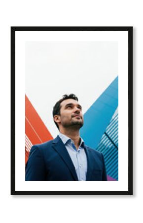Visionary businessman in blue suit looking up at colorful geometric background. Male executive inspiration concept for corporate motivation and business leadership