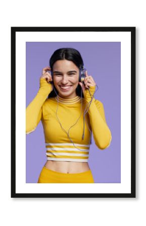 sport fitness woman smiling and enjoying music wearing yellow activewear with headphones against purple background, healthy lifestyle, workout motivation