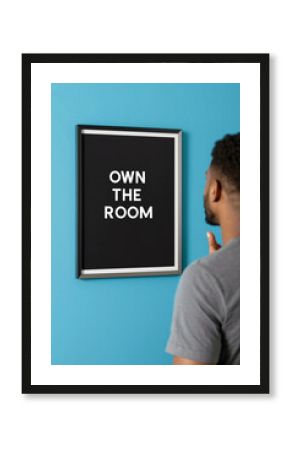 Man facing 'Own the Room' frame on blue wall