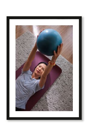 Woman lifting fitness ball while lying on yoga mat indoors