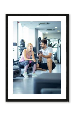 Mid adult woman and personal fitness trainer having conversation during workout break at gym.