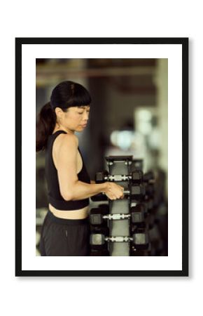 Focused Woman Selecting Dumbbells in a Modern Gym Setting
