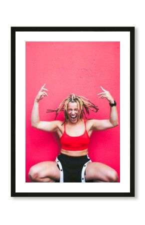 Athletic woman with dreadlocks showing attitude against red wall