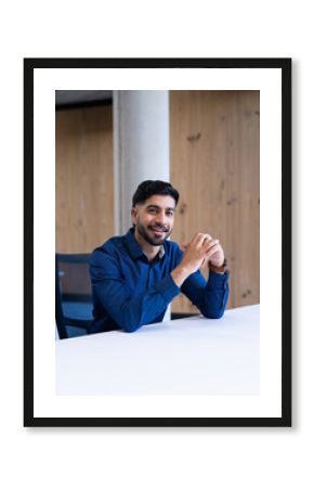 Smiling businessman in blue shirt sitting at desk in modern office, copy space