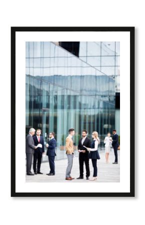 Groups of contemporary business people in formalwear standing by modern building and consulting outdoors