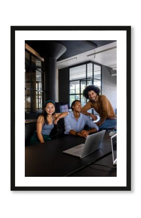 In office, diverse business team collaborating around laptop, smiling confidently