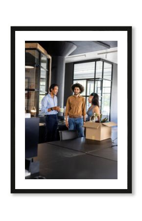 Colleagues in modern office chatting and smiling near unpacked box on desk