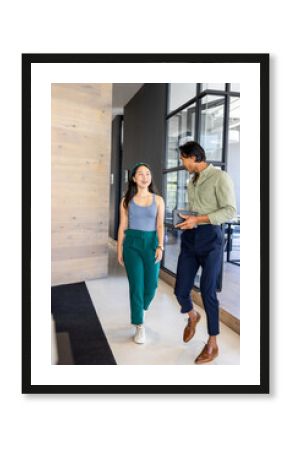 Asian colleagues walking in modern office, discussing work with smiles