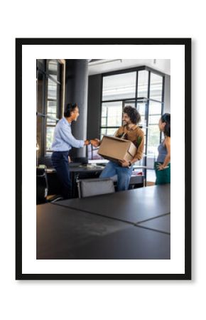 Colleagues welcoming new team member with handshake and box in modern office