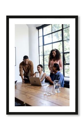 Diverse business team collaborating on laptop in modern office, smiling and engaged