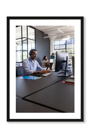 In office, businessman using computer and headset, collaborating with colleagues