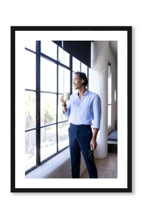 Businessman enjoying coffee break while looking out office window, feeling relaxed