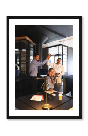 Team celebrating success in modern office, high-fiving and smiling at desk