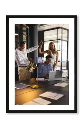 Colleagues celebrating success at office, smiling and high-fiving near laptop