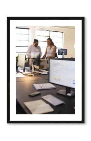 Colleagues discussing project at modern office desk with computer and documents