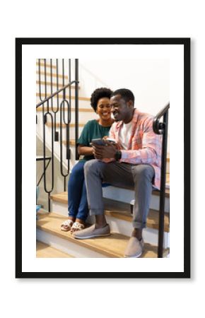 Smiling friends sitting on stairs, sharing smartphone and enjoying coffee together