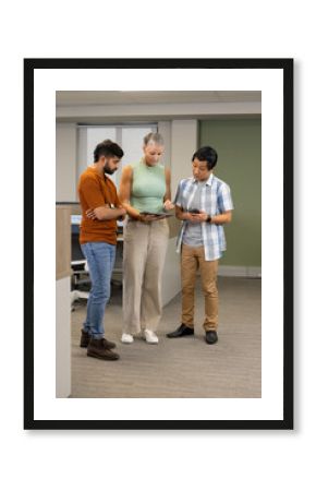 Diverse office colleagues standing and reviewing tablet in modern open-plan office, with smartphone