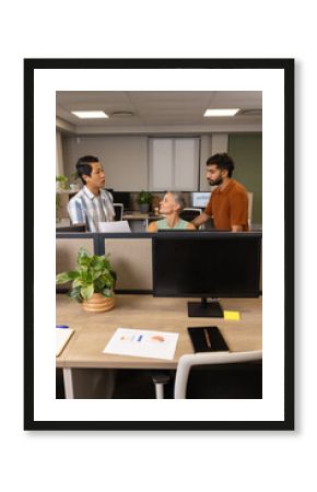 Discussing strategy diverse colleagues standing at desk in office, with printed charts and monitors