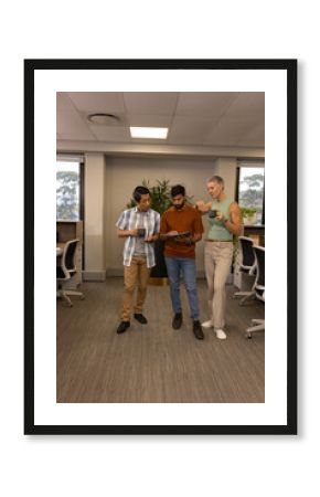 Standing Diverse colleagues reviewing content on tablet in office corridor, with coffee mugs